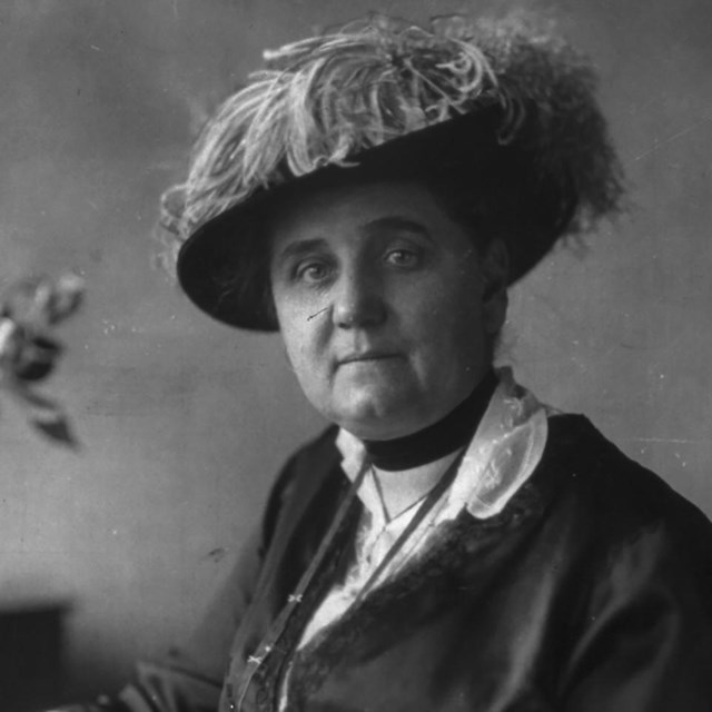 Portrait photograph of Jane Addams seated at a desk, holding a pen.