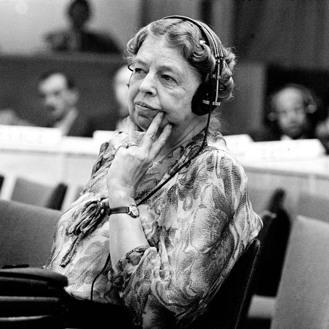A woman with headphones listens to speakers at an assembly.
