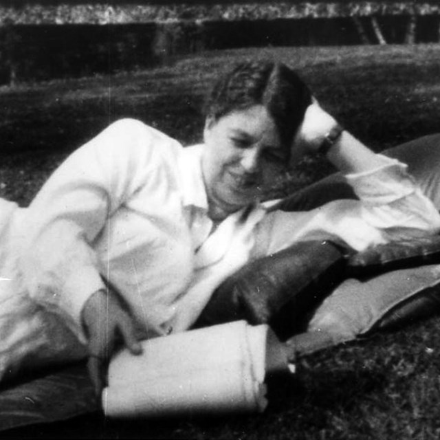 A woman in a white dress reclining on a lawn with a book.
