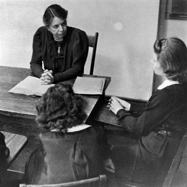 A woman at a desk conducting a class with three girls.
