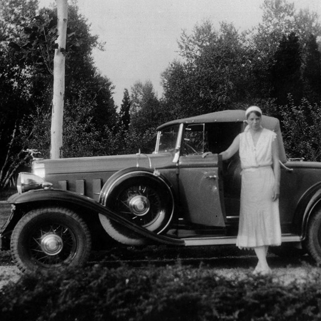 A woman in summer whites standing near an automobile.