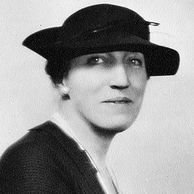 A woman in a dark dress and hat.