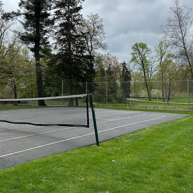 A tennis court with net and wire fence backdrop.
