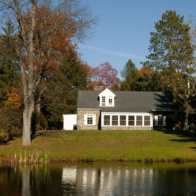 A fieldstone cottage on the edge of a large pond.