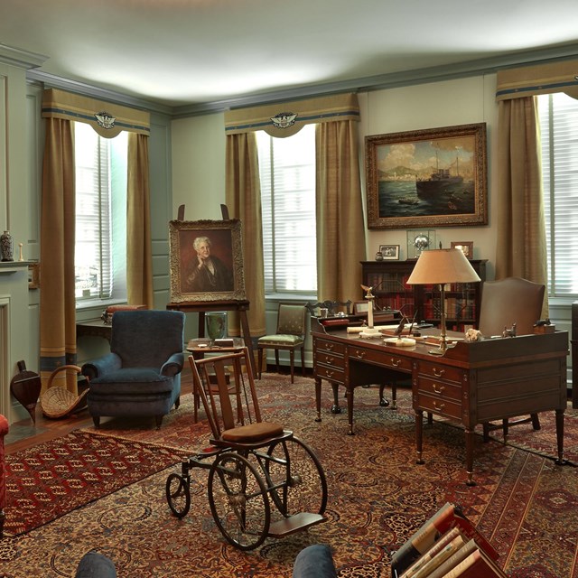 A room with fireplace, cozy furniture, desk, and a wheel chair at center.