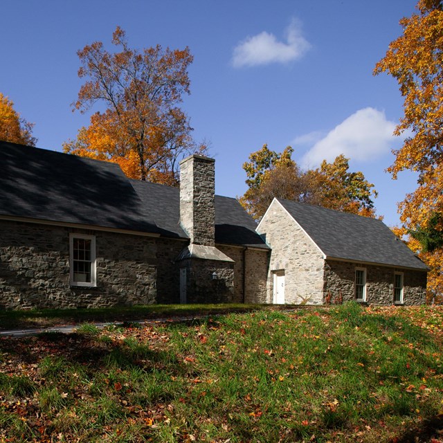 A stone house with steep pitched roof atop a gentle hill.