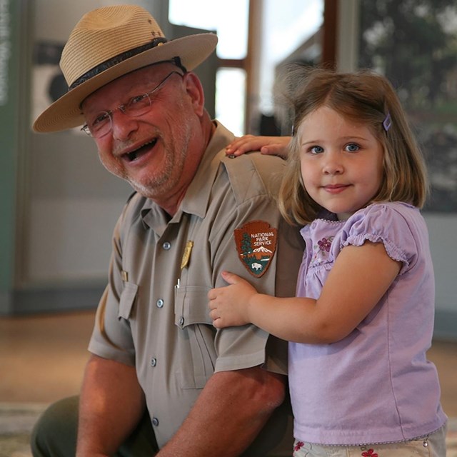 A park ranger with a young girl smiles at the camera.