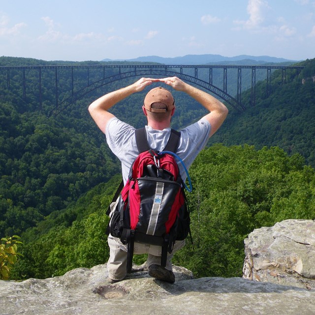 Visitor looking out at a bridge over the New River Gorge, mimicking its shape with his arms