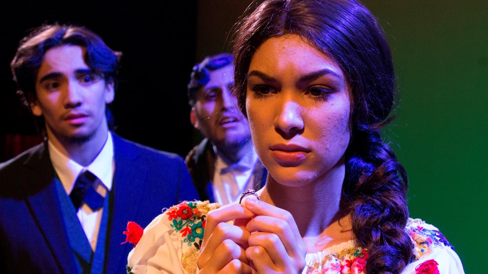 Una mujer vestida en ropa tradicional de México está enfrente con dos hombres de fondo.