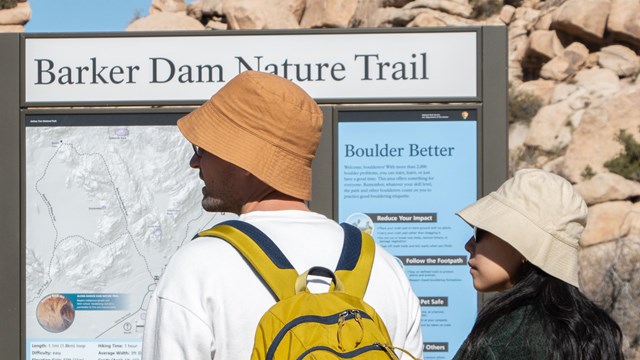 Dos visitantes del parque frente al tablero informativo en la entrada del sendero de Barker Dam