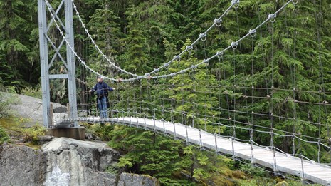 Un excursionista cruza un largo puente colgante sobre un cauce rocoso.