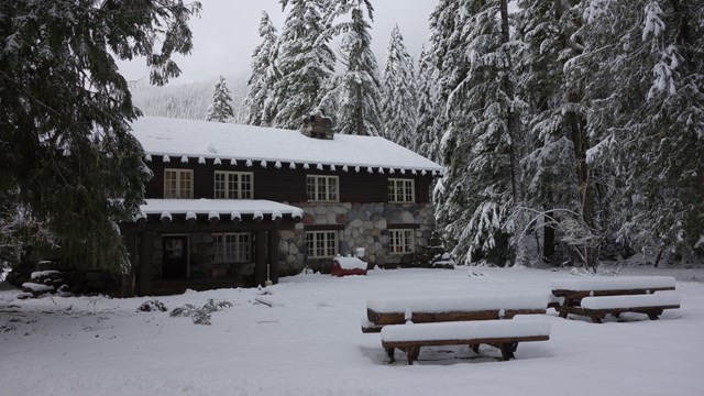 Un edificio de madera y piedra inmerso en el bosque y cubierto de nieve.