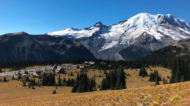 Un conjunto de edificios en un prado dorado junto a una montaña cubierta de glaciares.
