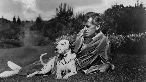 Historic photograph and Eugene O'Neill laying in the grass with dog, Blemie. 