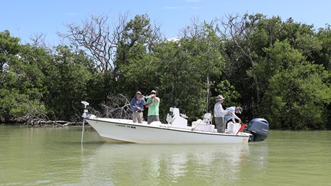 A boat with 4 anglers in murky water in front of a vegetated island