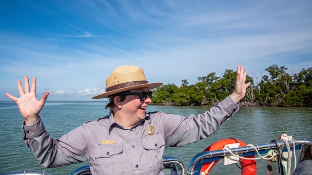 A Park Ranger on a boat holds our their arms, expressing joy.