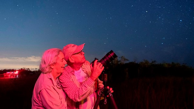 Two people stand by a camera pointed up at a dark night sky.