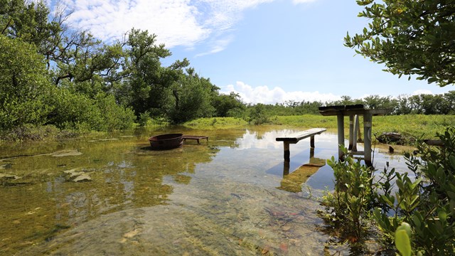 A flooded campground showing a picnic table and fire ring in several inches of water.