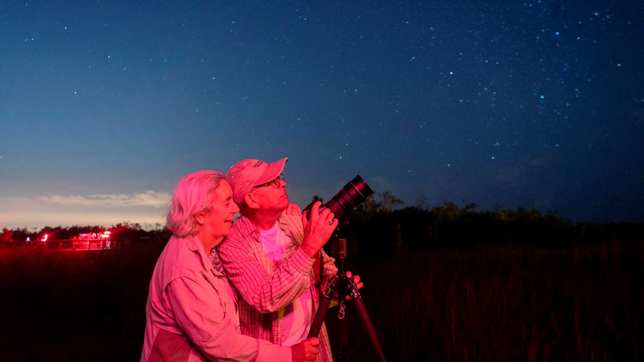 Two people stand by a camera pointed up at a dark night sky.