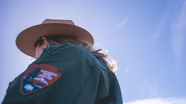 The NPS arrowhead and ranger's flat hat against a blue sky.