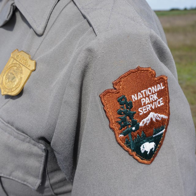 A close up of a gray uniform with the National Park Service arrowhead and badge