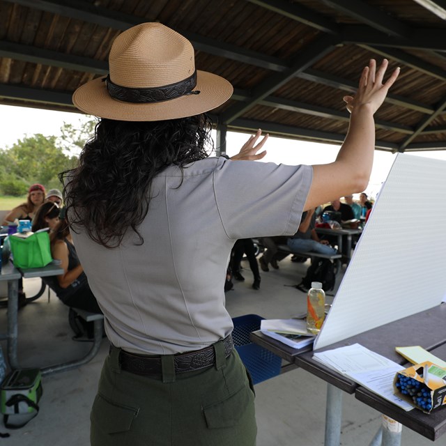 A female Park Ranger addresses a group of visitors under a sheltered area outdoors