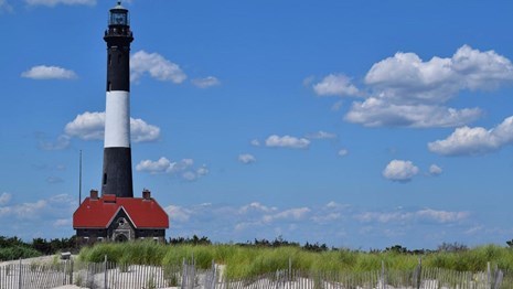 black and white striped lighthouse with dunes and tall grass in the foreground