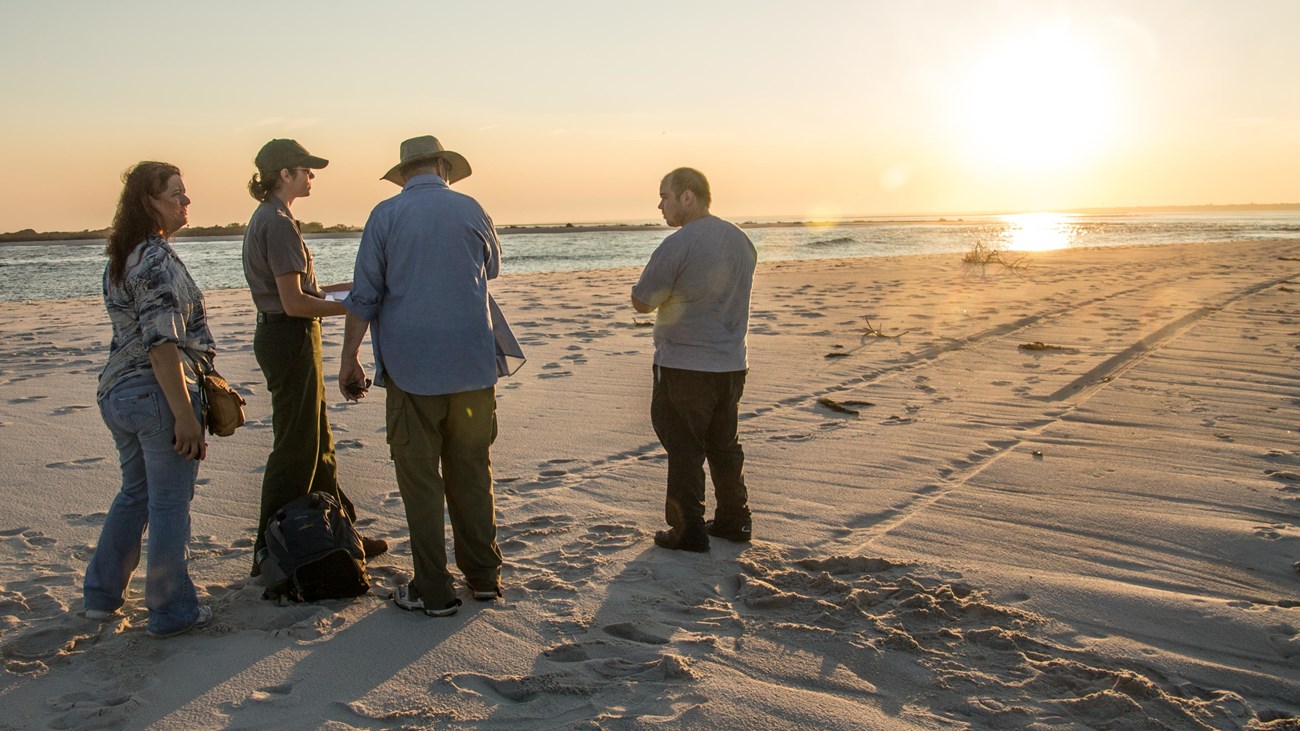 A group stands by the breach channel at sunset.