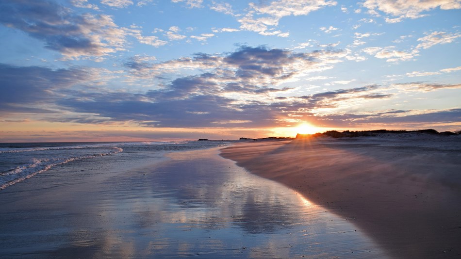 Sunset reflecting in wave wash-up on sandy beach.
