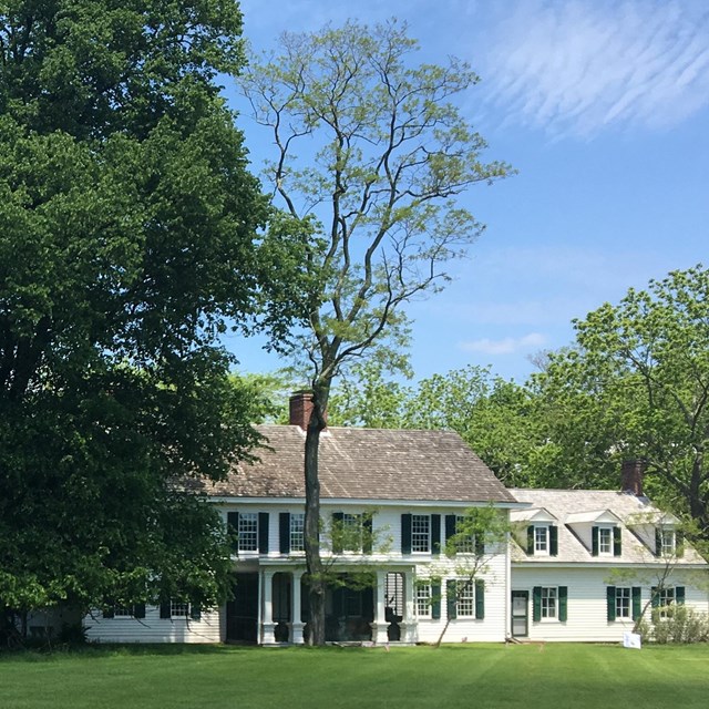 Large, white historic home surrounded by lush green lawn and trees.