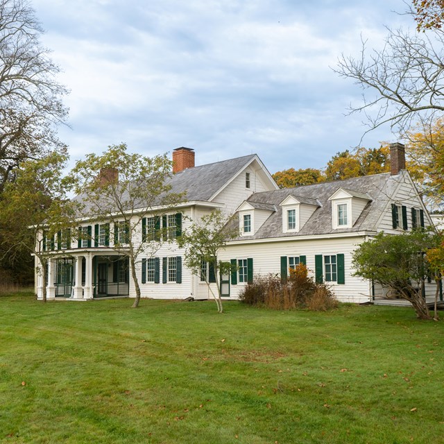 A house with white and green shutters on a grassy field.