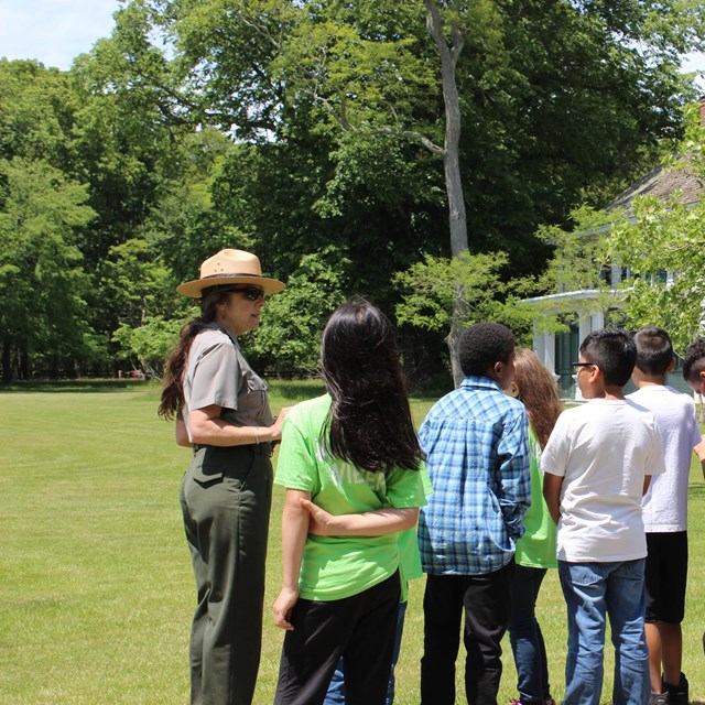 People walk on a lawn near an historic home.