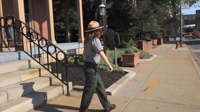 a park ranger walks down a set of stairs to a side walk close to a city street. 