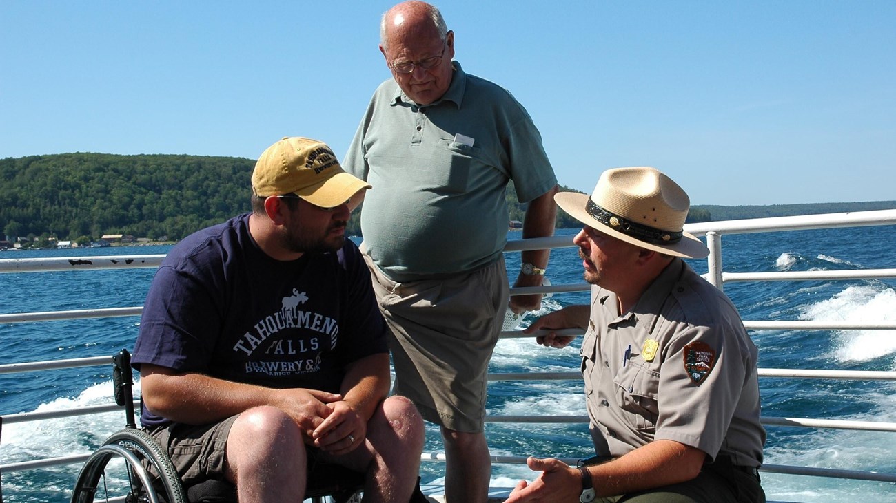 A ranger squats next to a visitor in a wheel chair and talks 