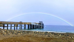 A beach and a pier with a rainbow in the back
