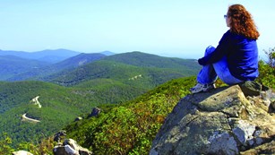Hiker sitting on a rock overlooking a mountain valley
