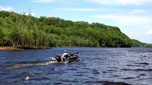 man on a small boat cruising on a lake with trees in the background