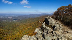 Rocky outcrop on top of a mountain ridge covered with colorful trees