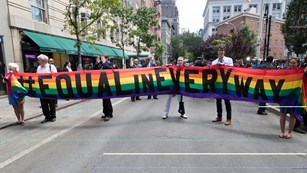 a few people holding a long horizontal rainbow sign with the words 'equal in every way'