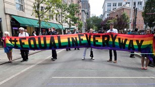 Group of people standing with long rainbow banner that says