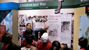 Ranger talking to school group in front of a museum exhibit about children during war