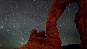 Geological arch with star trails behind it