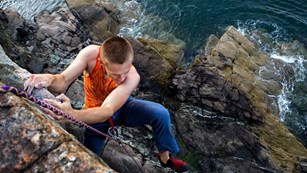 man rock climbing on a cliff with water underneath
