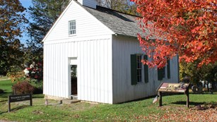 A small, white, wooden chapel among autumn-tinged trees.
