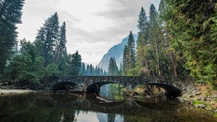 Stone bridge over a river near trees and mountains