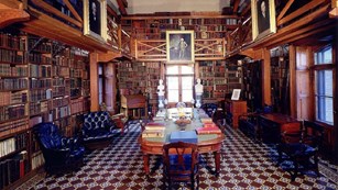 Library room with many shelves of books and a table lined with chairs