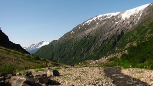 image of a mountain with some snow left, a river and some rocks around it