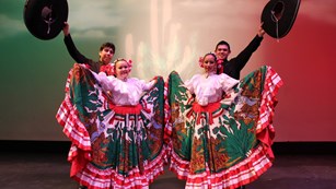 Two sets of dancers on stage showing large colorful skirts