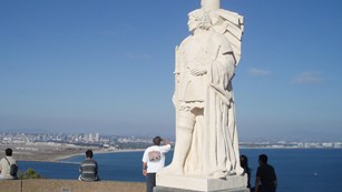 Tall white statue of Cabrillo with shoreline in background.