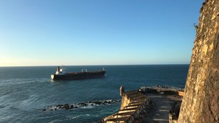 Ships entering a bay near a stone fort wall
